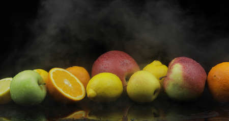 Tropical lemon, orange, apple in cold ice clouds of fog smoke on black background. Fresh and tasty fruits. Concept of healthy and rich in vitamins foodの写真素材
