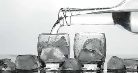 Pouring up shot of vodka into glass with ice against black background. Pour of alcohol drink vodka tequilaの写真素材