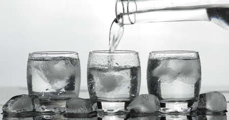 Pouring up shot of vodka into glass with ice against black background. Pour of alcohol drink vodka...