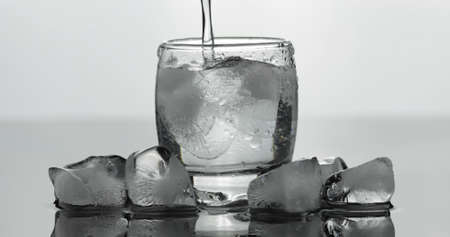 Pouring up shot of vodka into glass with ice against black background. Pour of alcohol drink vodka tequilaの写真素材