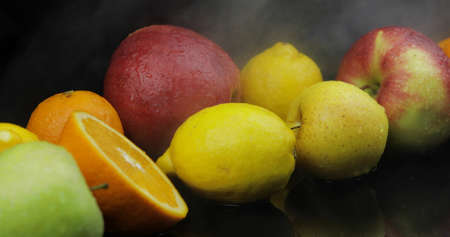 Tropical lemon, orange, apple in cold ice clouds of fog smoke on black background. Fresh and tasty fruits. Concept of healthy and rich in vitamins foodの写真素材