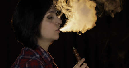 Beautiful, young woman smoking hookah. Attractive girl smoking flavored tobacco. Blow out smoke on black backgroundの写真素材
