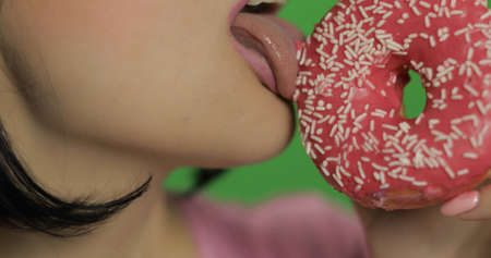 Cute woman licking colorful sprinkled sweet donut. Happy beautiful young girl on a chroma key background with donuts. Close-up shotの写真素材