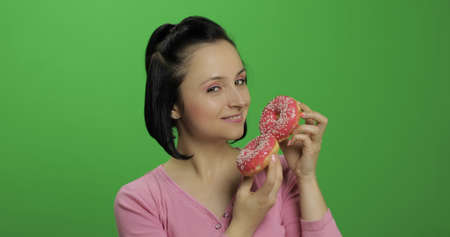 Happy beautiful young girl on a chroma key background having fun with donuts. Cute woman in a pink shirt posing with donuts. Making facesの写真素材