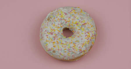 Delicious, tasty and fresh donut. Top view. Bright and colorful sprinkled white sweet donut close-up macro shot on a pink backgroundの写真素材