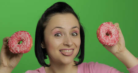 Happy beautiful young girl on a chroma key background having fun with donuts. Cute woman in a pink shirt posing with donuts. Making facesの写真素材