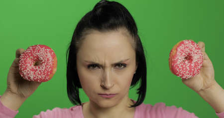 Happy beautiful young girl on a chroma key background having fun with donuts. Cute woman in a pink shirt posing with donuts. Making facesの写真素材