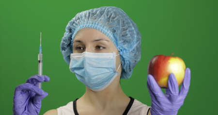 Female scientist holding syringe with medicines in one hand and an apple in other hand. She chooses syringe with medicines. Concept of medicine method of treatment. Chroma key backgroundの写真素材
