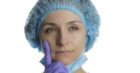 Close-up young doctor is thinking. Adult female medical worker in face mask holding chin on hand and looking thoughtful. Searching a right solution. White backgroundの写真素材