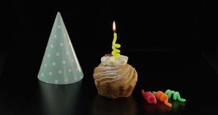 Party. Cake and a yellow festive candle on it. Colored party hat. Black background. Celebrate an event, birthdayの写真素材