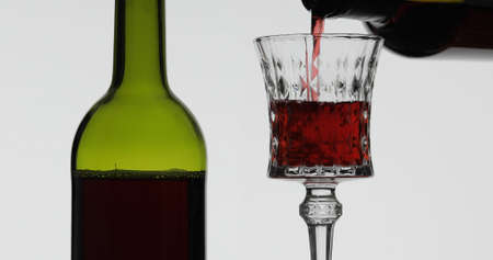 Wine. Red wine pouring in wine glass over white background. Rose wine pour from the bottleの写真素材