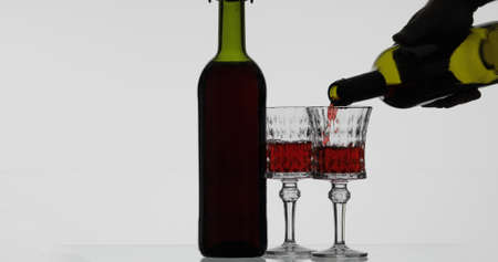 Wine. Red wine pouring in wine glass over white background. Rose wine pour from the bottleの写真素材