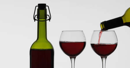 Wine. Red wine pouring in wine glass over white background. Rose wine pour from the bottle
