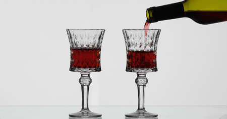 Wine. Red wine pouring in wine glass over white background. Rose wine pour from the bottleの写真素材