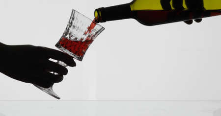 Wine. Red wine pouring in wine glass over white background. Rose wine pour from the bottle