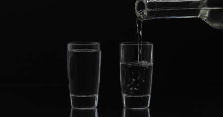 Pouring up shot of vodka from a bottle into glass against black background. Pour of alcohol drink...