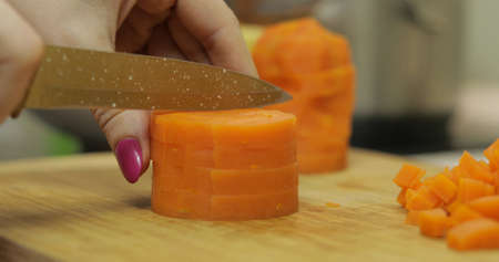Female housewife hands slicing carrots into pieces on the wooden cutting board in the kitchenの写真素材