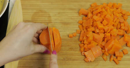 Female housewife hands slicing carrots into pieces on the wooden cutting board in the kitchenの写真素材