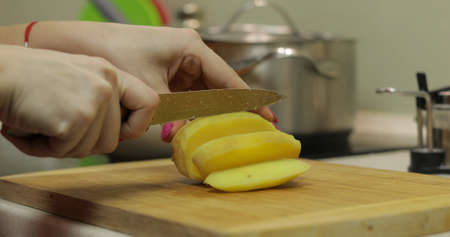 Female housewife hands slicing potatoes into pieces on the wooden cutting board in the kitchenの写真素材