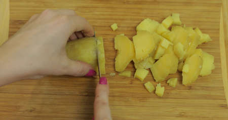 Female housewife hands slicing potatoes into pieces on the wooden cutting board in the kitchenの写真素材