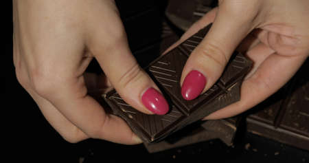 Woman holds black chocolate bar. Close-up shot of woman fingers with the chocolateの写真素材