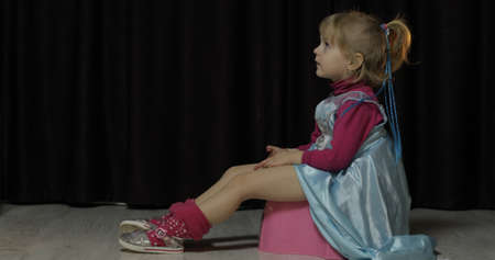 Little girl sitting on the potty and watching TV. Blonde cute child in blue dress. Insideの写真素材