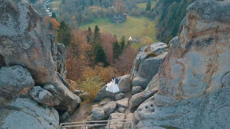 Wedding couple stand on a high slope of the mountain hills. Lovely groom and bride. Man and woman in love. Wedding day. Arial view. Shot from droneの写真素材