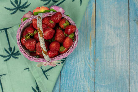 Strawberries in a small basket on the blue wooden background - close up. Place for your logo or textの写真素材
