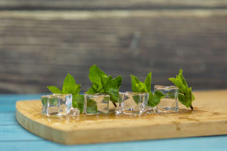Ice cubes and fresh mint leaves isolated on wooden cutting board.
