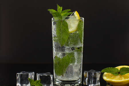 Clear water in glass with green mint leaves and ice cubes on black background.