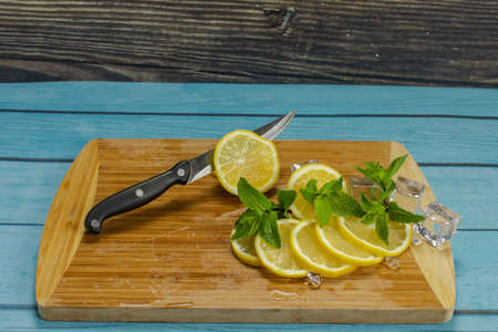 Sliced lemon for mojito cocktail on a wooden cutting board in the kitchen. Ice cubes and fresh mint...