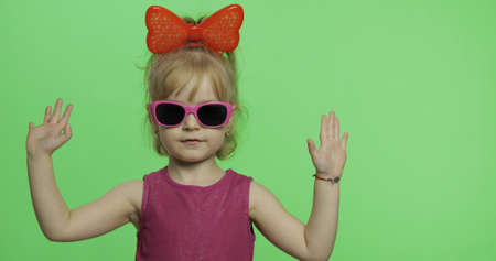 Positive girl in purple dress, sunglasses and red ribbon looking at camera. Makes a stop symbol....