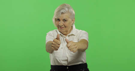 An elderly woman show thumb up and smiles. Old pretty grandmother in a white shirt. Place for your...