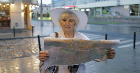 Senior female tourist exploring town with a map in hands and looking for the route while traveling in Lviv, Ukraine. Elegant woman in hat with binoculars. Vacation conceptの写真素材