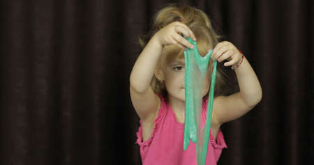 Child having fun making green slime. Kid playing with hand made toy slime. Funny kid girl. Blowing bubble via the drinking straw. Oddly satisfying blue slime for pure fun and stress reliefの写真素材