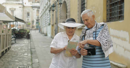 Senior two male and female tourists in city center. Traveling in Lviv, Ukraine. Elegant woman in hat with handsome man with photo camera. Family vacation conceptの写真素材