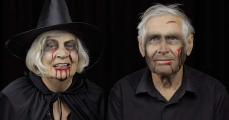 Elderly man and woman in Halloween costumes. Dripping blood on their faces. Witch, vampire, zombie makeup. Fashion art design. Attractive models. Black backgroundの写真素材