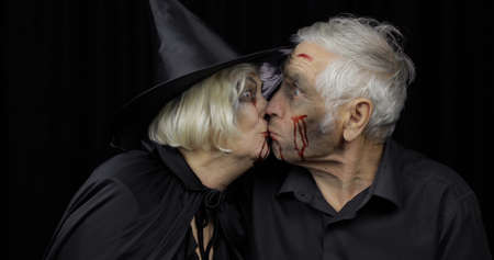 Elderly man and woman in Halloween costumes making a kiss. Dripping blood on their faces. Witch, vampire, zombie makeup. Fashion art design. Attractive models. Black backgroundの写真素材