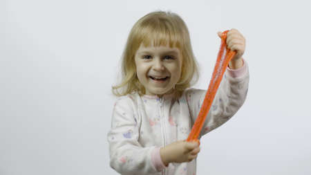 Child having fun making orange slime. Kid playing with hand made toy slime. Funny kid girl. Relax and Satisfaction. Oddly satisfying orange slime for pure fun and stress relief. White backgroundの写真素材