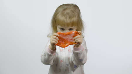 Child having fun making orange slime. Kid playing with hand made toy slime. Funny kid girl. Relax and Satisfaction. Oddly satisfying orange slime for pure fun and stress relief. White backgroundの写真素材