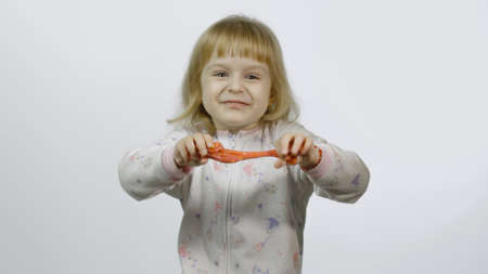 Child having fun making orange slime. Kid playing with hand made toy slime. Funny kid girl. Relax and Satisfaction. Oddly satisfying orange slime for pure fun and stress relief. White backgroundの写真素材