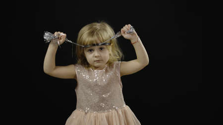 Happy beautiful little baby girl in glossy dress. Christmas concept. Positive, pretty, four years old child make faces, dance and smile. Black backgroundの写真素材