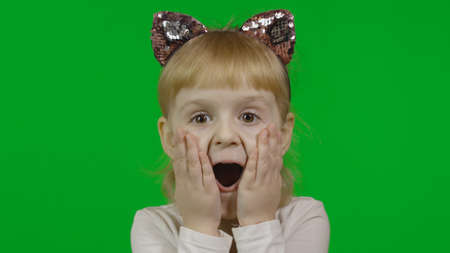 Girl in headband with a cats ears shows emotion of amazement. Happy four years old girl. Pretty little blonde child. Make faces and smile. Green screen. Chroma Keyの写真素材