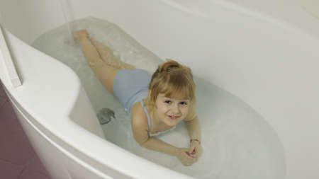 Attractive four years old girl takes a bath in swimwear. Hygiene for cute blonde child. Cute girl...