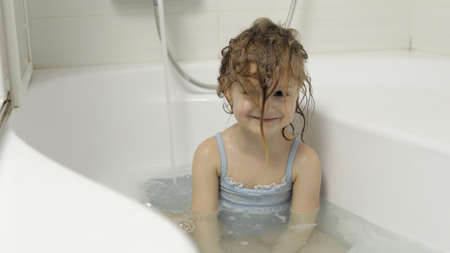 Attractive four years old girl takes a bath with bath foam in swimwear. Washes her head. Wet hair....
