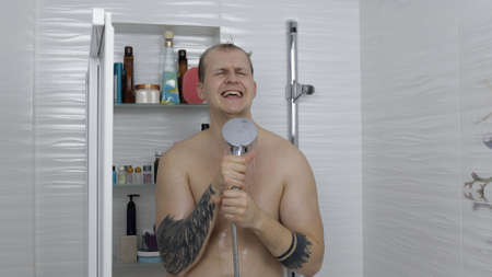 Young handsome fat man takes a shower at bathroom. The guy with tattoos washes his body. Emotionally...