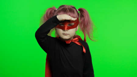 Cute baby girl plays superhero. Make faces, hand over eyes. Funny child in homemade costume of super hero with red cape and mask. National superhero day concept. Portrait close up. Chroma keyの写真素材