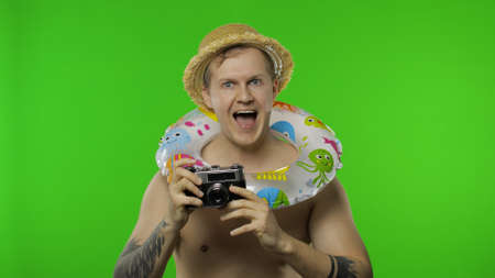 Shirtless young happy man tourist photographer is taking photos on retro camera. Portrait of blonde...