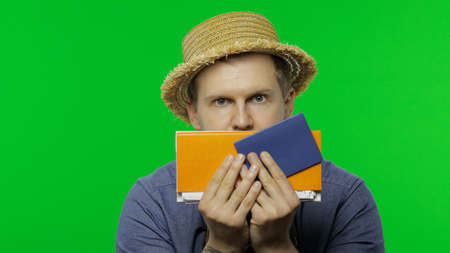 Portrait of man tourist hides behind a passport and tickets and looks out. Handsome man in blue...