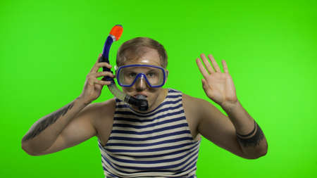 Emotional handsome guy tourist in underwater swimming goggles mask wear striped sailor shirt vest and with breathing tube. Chroma key. Muscular sailor man waving hands. Concept of tourism, sea resortsの写真素材
